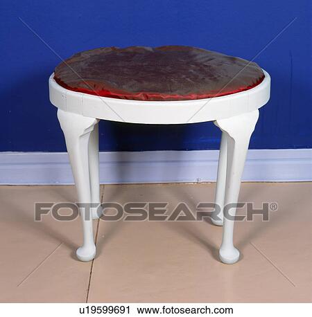 Stock Image - Close-up of white painted stool with red silk seat. Fotosearch