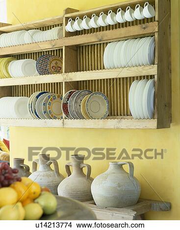 Close-up of white plates and cups on wooden plate-rack above Greek pots in yellow kitchen View Large Photo Image Picture - Close-up of white plates and cups on wooden plate-rack above Greek pots in yellow kitchen. Fotosearch