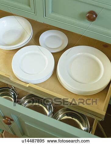Stock Photography - Close-up of white plates in storage drawer in pastel green kitchen cupboard. Fotosearch