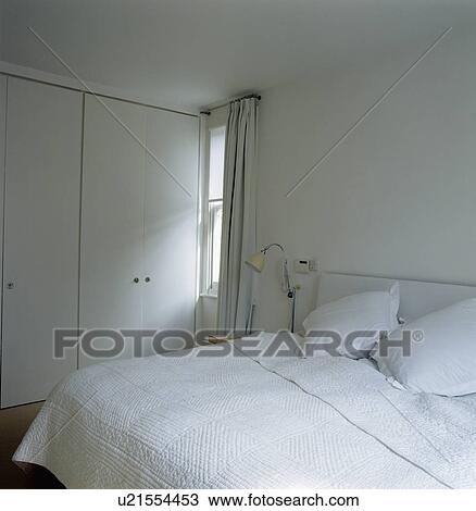 Close-up of white quilt and pillows on bed in white bedroom with fitted wardrobe View Large Photo Image Stock Image - Close-up of white quilt and pillows on bed in white bedroom with fitted wardrobe. Fotosearch