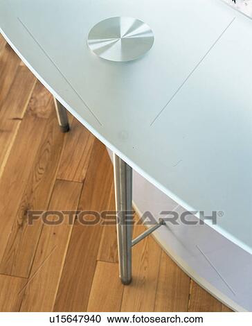 Stock Image - Close-up of white table with stainless steel legs on wooden flooring. Fotosearch
