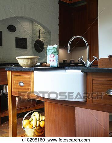 Stock Image - Close-up of whyite sink and chrome tap in fitted wood kitchen unit. Fotosearch