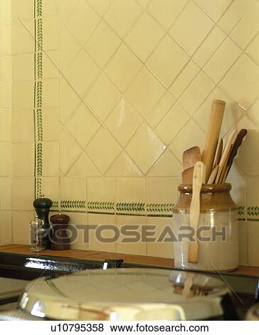 Stock Photo - Close-up of wooden utensils in jar below cream wall tiles laid in a diamond pattern. Fotosearch