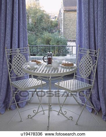Stock Photograph - Coffee and croisants on white metal table with matching chairs in front of window with blue curtains . Fotosearch