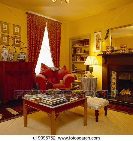Coffee-table piled with books in traditional yellow living room with patterned red curtains and lighted lamp View Large Photo Image Stock Image - Coffee-table piled with books in traditional yellow living room with patterned red curtains and lighted lamp. Fotosearch