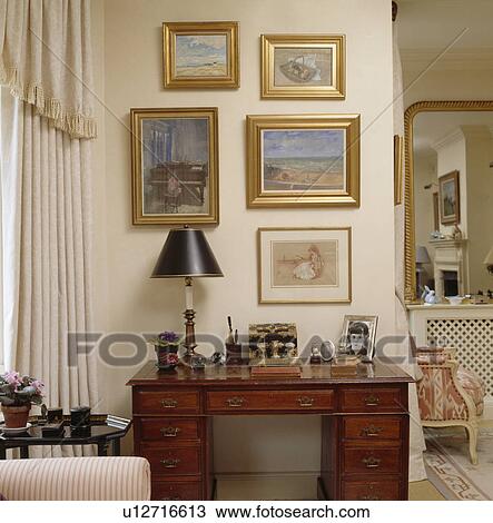 Collection of pictures above lamp on antique desk in traditional neutral livingroom View Large Photo Image Stock Image - Collection of pictures above lamp on antique desk in traditional neutral livingroom. Fotosearch
