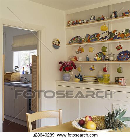 Stock Photo - Colourful crockery on shelves in dining room with open door to kitchen. Fotosearch