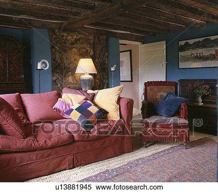 Stock Photography - Comfortable pink sofa and antique velvet chair in beamed country living room. Fotosearch