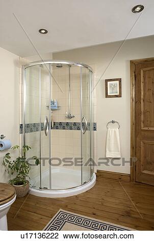 Stock Image - Corner shower cabinet with glass doors in cream bathroom with wooden flooring. Fotosearch