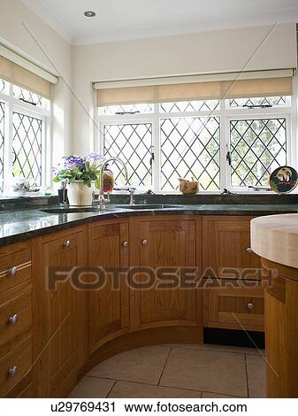 Stock Image - Corner sink below lattice windows in cottage kitchen with fitted wood units. Fotosearch
