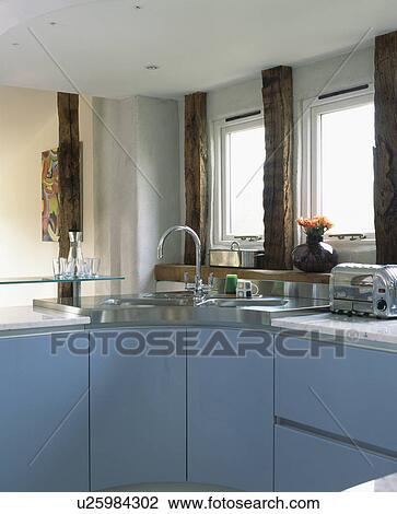 Stock Image - Corner sink in pale blue fitted units in modern country kitchen. Fotosearch