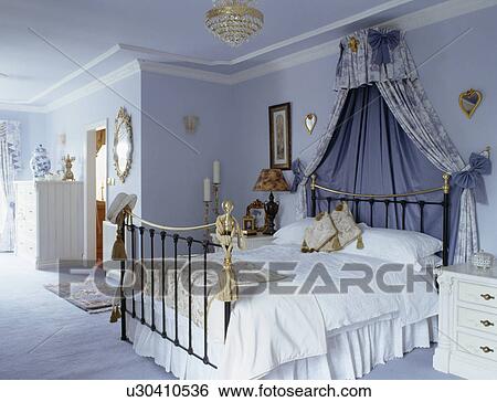 Coronet With Blue Drapes Above Brass Bed In Pastel Blue Bedroom