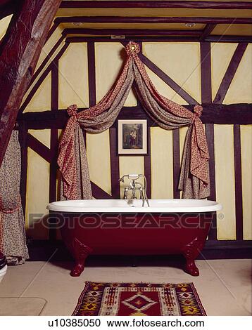 Coronet with red drapes above red roll-top bath in beamed country bathroom View Large Photo Image Stock Image - Coronet with red drapes above red roll-top bath in beamed country bathroom. Fotosearch