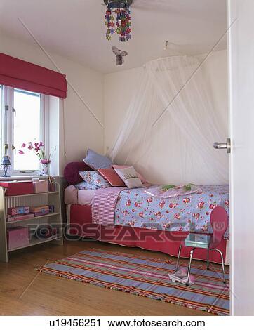 Stock Image - Coronet with white voile drapes above bed with blue bedlinen and red valence . Fotosearch