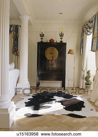 Stock Photo - Cow-hide rug and oriental cupboard in country living room with classical column. Fotosearch