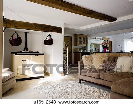 Stock Image - Cream Aga oven in country kitchen with brown suede sofa and cream faux-fur cushions. Fotosearch