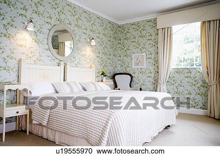 Cream Bedline On Bed In Country Bedroom With Cream Curtains And Green And Pale Blue Patterned Wallpaper Stock Image