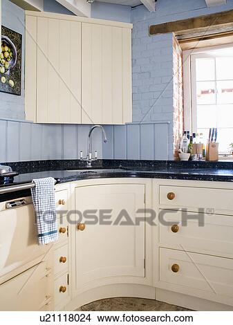 Cream corner cupboard above sink in pale blue country kitchen with cream fitted cupboards and units View Large Photo Image Picture - Cream corner cupboard above sink in pale blue country kitchen with cream fitted cupboards and units. Fotosearch