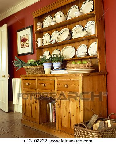 Stock Image - Cream crockery on pine dresser in red country kitchen. Fotosearch