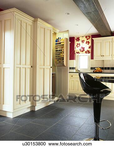 Cream fitted larder cupboard in country kitchen with black ceramic floor tiles and black Bomba stool View Large Photo Image Stock Image - Cream fitted larder cupboard in country kitchen with black ceramic floor tiles and black Bomba stool. Fotosearch