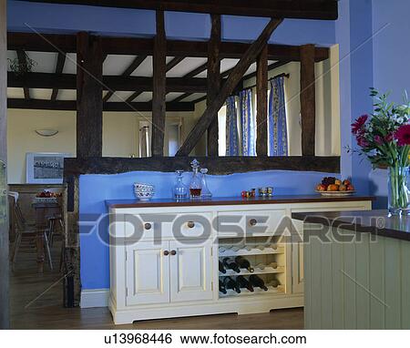 Stock Photograph - Cream fitted unit in front of wall with plaster removed to expose upright beams in blue country kitchen. Fotosearch