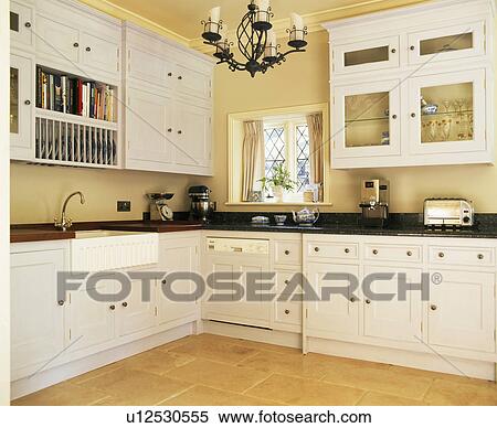Stock Photography - Cream fitted units and cupboards in country kitchen. Fotosearch