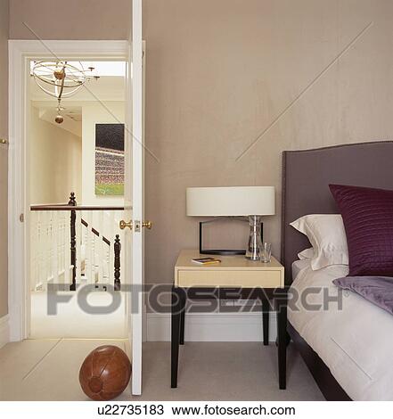 Cream lamp on modern bedside table between bed and open door in modern beige bedroom View Large Photo Image Stock Image - Cream lamp on modern bedside table between bed and open door in modern beige bedroom. Fotosearch