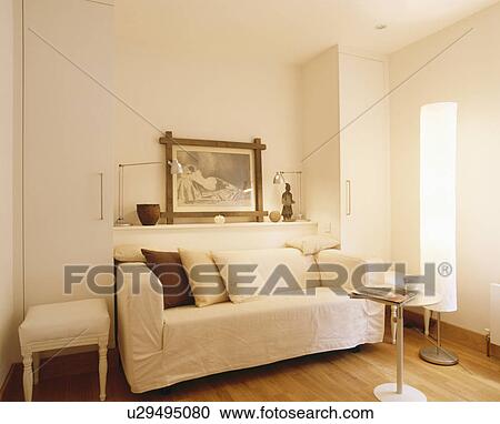 Stock Image - Cream loosecover on sofabed in modern white living room. Fotosearch