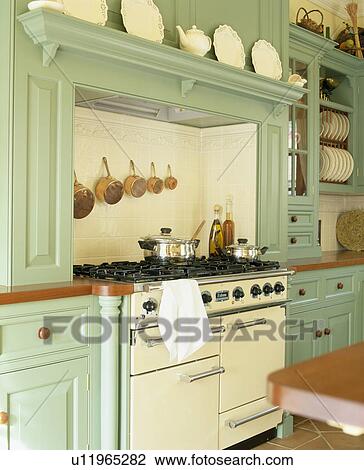 Stock Image - Cream range oven traditional country kitchen with pale green fitted units. Fotosearch
