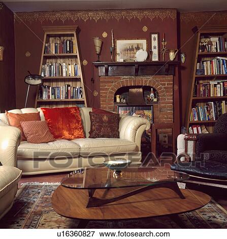 Cream sofa and fifties table in terracotta living room with gold stencilled border on walls and freestanding bookshelves View Large Photo Image Stock Photo - Cream sofa and fifties table in terracotta living room with gold stencilled border on walls and freestanding bookshelves. Fotosearch
