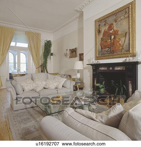 Cream sofas and modern glass table in traditional living room with large picture above fireplace View Large Photo Image Stock Photo - Cream sofas and modern glass table in traditional living room with large picture above fireplace. Fotosearch