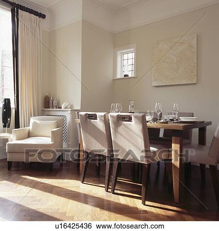 Stock Photograph - Cream upholstered chairs and simple wooden table in neutral dining room with cream armchair and wooden flooring. Fotosearch