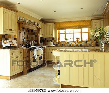 Stock Image - Cream wooden units in pale yellow country kitchen with limestone flooring and range oven. Fotosearch
