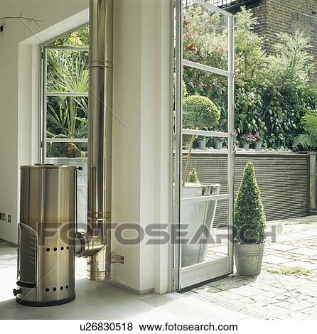 Stock Photo - Cylindrical stainless steel stove beside open glass doors to townhouse patio. Fotosearch