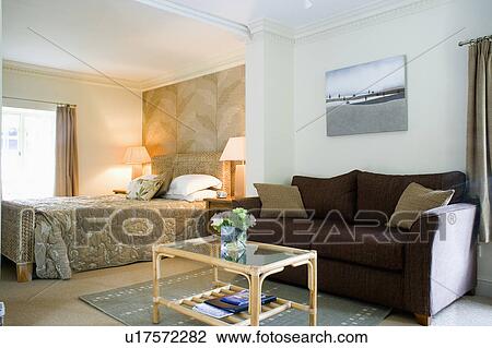 Stock Image - Dark grey sofa and cane+glass table in traditional bedroom. Fotosearch