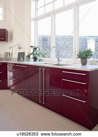 Stock Image - Dark wood fitted units below window in modern kitchen. Fotosearch