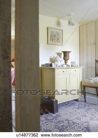 Stock Image - Door open to cottage bedroom with small wooden cupboard and patterned blue carpet. Fotosearch