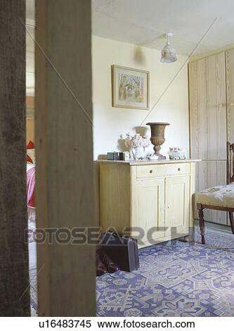 Stock Photography - Door open to cottage bedroom with small wooden cupboard and patterned blue carpet. Fotosearch