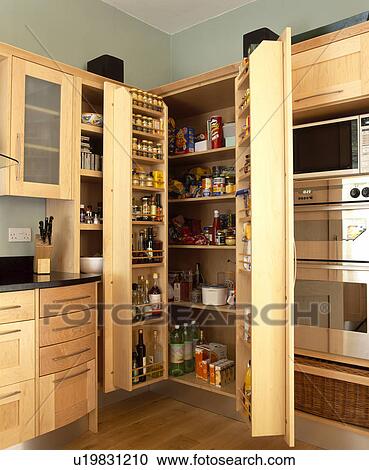 Stock Image - Double doors open on larder cupboard in modern fitted kitchen with pale wood units. Fotosearch