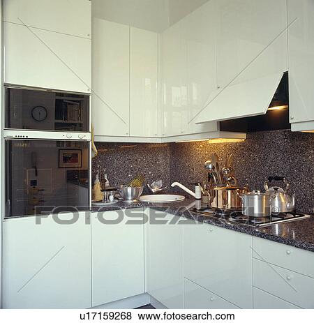 Stock Photo - Double oven and hob in fitted units in compact modern white kitchenwith black granite splashback. Fotosearch