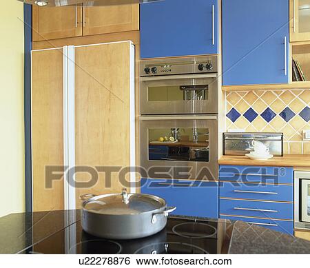 Double oven in fitted blue units in modern kitchen with concealed fridge-freezer behind pale wood doors View Large Photo Image Stock Photograph - Double oven in fitted blue units in modern kitchen with concealed fridge-freezer behind pale wood doors. Fotosearch