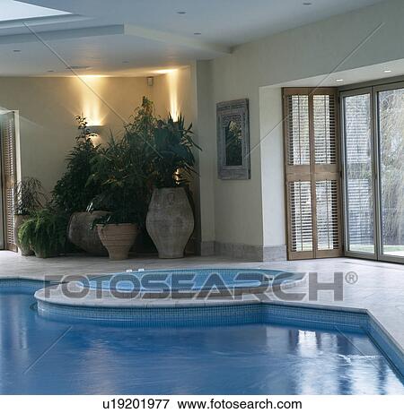 Stock Photo - Down-lighting above houseplants in modern indoor swimming pool and hot tub. Fotosearch