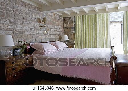 Exposed stone wall behind bed with pink blankets in cottage bedroom with pastel green curtains View Large Photo Image Stock Photograph - Exposed stone wall behind bed with pink blankets in cottage bedroom with pastel green curtains. Fotosearch