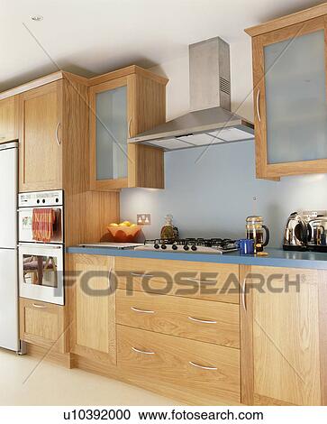 Stock Image - Extractor fan above hob in pale wood fitted units in modern kitchen. Fotosearch