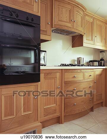 Stock Photograph - Eye-level oven in fitted cherry-wood unit in modern kitchen. Fotosearch