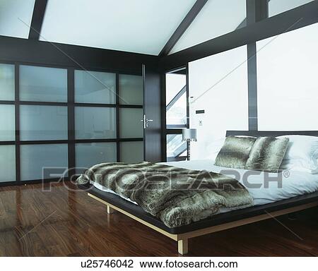 Faux fur throw and cushions on bed in modern bedroom with opaque glass panelled wall and black beams View Large Photo Image Stock Image - Faux fur throw and cushions on bed in modern bedroom with opaque glass panelled wall and black beams. Fotosearch