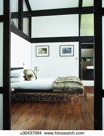 Faux fur throw on bed in modern bedroom with wooden flooring and black beams View Large Photo Image Picture - Faux fur throw on bed in modern bedroom with wooden flooring and black beams. Fotosearch