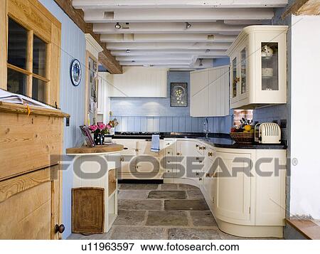 Stock Photo - Fitted cream units and flagstone floor in pastel blue country kitchen. Fotosearch
