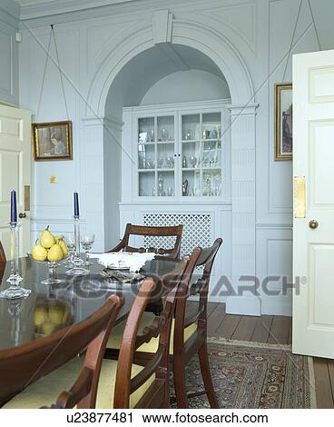 Stock Image - Fitted cupboard in alcove in traditional country dining room with antique table and chairs. Fotosearch
