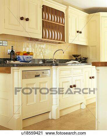 Stock Image - Fitted dishwasher below wall-cupboard with integral plate-rack in cream kitchen painted in Farrow+Ball paint. Fotosearch
